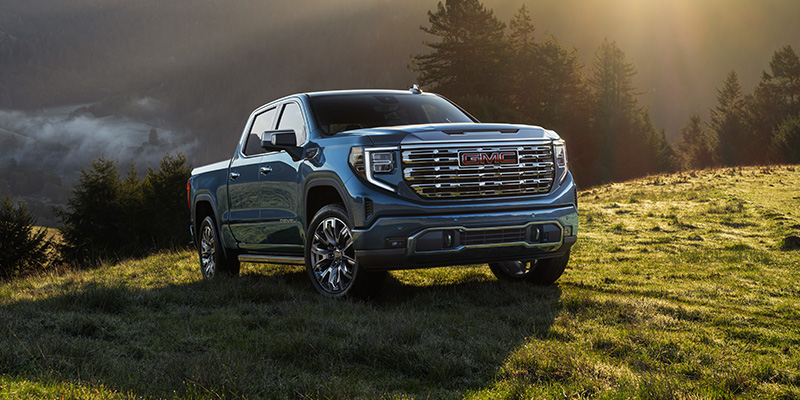 A blue GMC Sierra 1500 pickup truck parked on a grassy hillside at sunrise