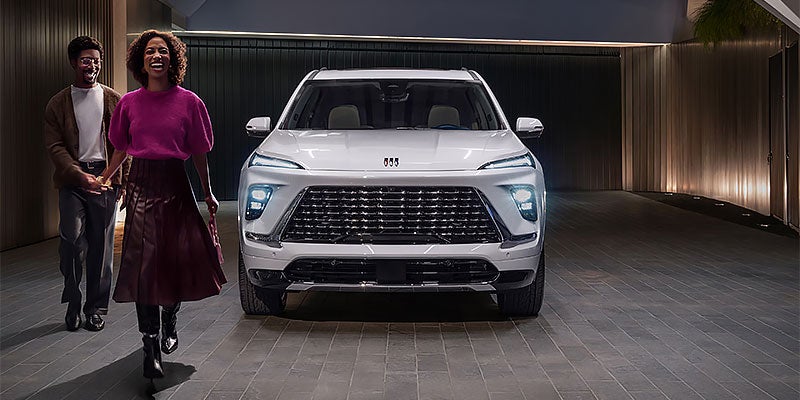 Two people walk beside a white Buick Enclave in a modern driveway.
